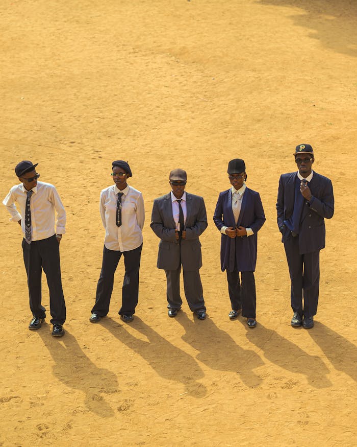 Aerial view of five men in formal attire casting long shadows on a sunlit sandy ground