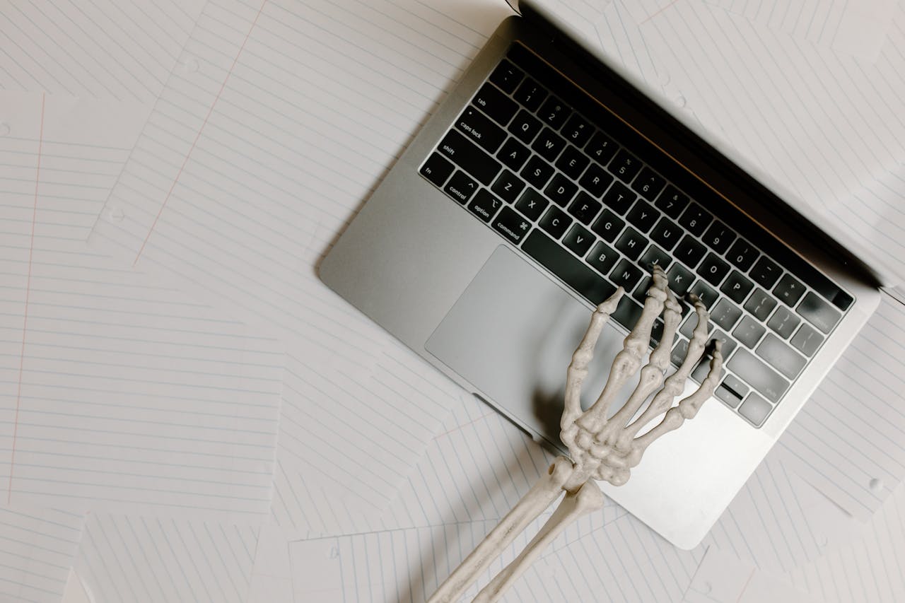 Skeleton hand on laptop keyboard overlaid on papers, symbolizing burnout.